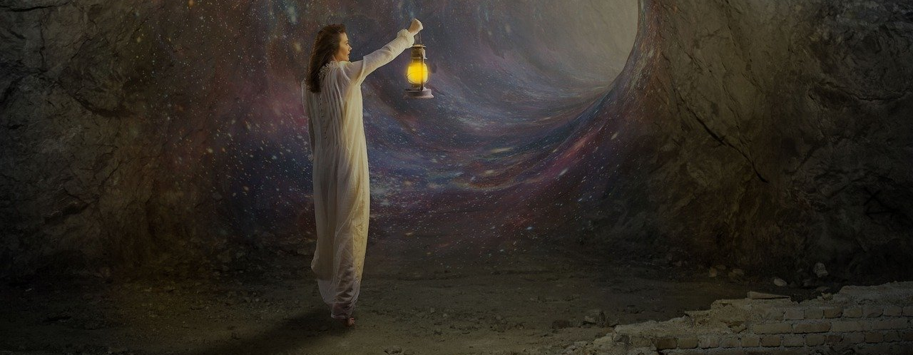 Woman is walking down a dark tunnel holding a gaslight lamp.