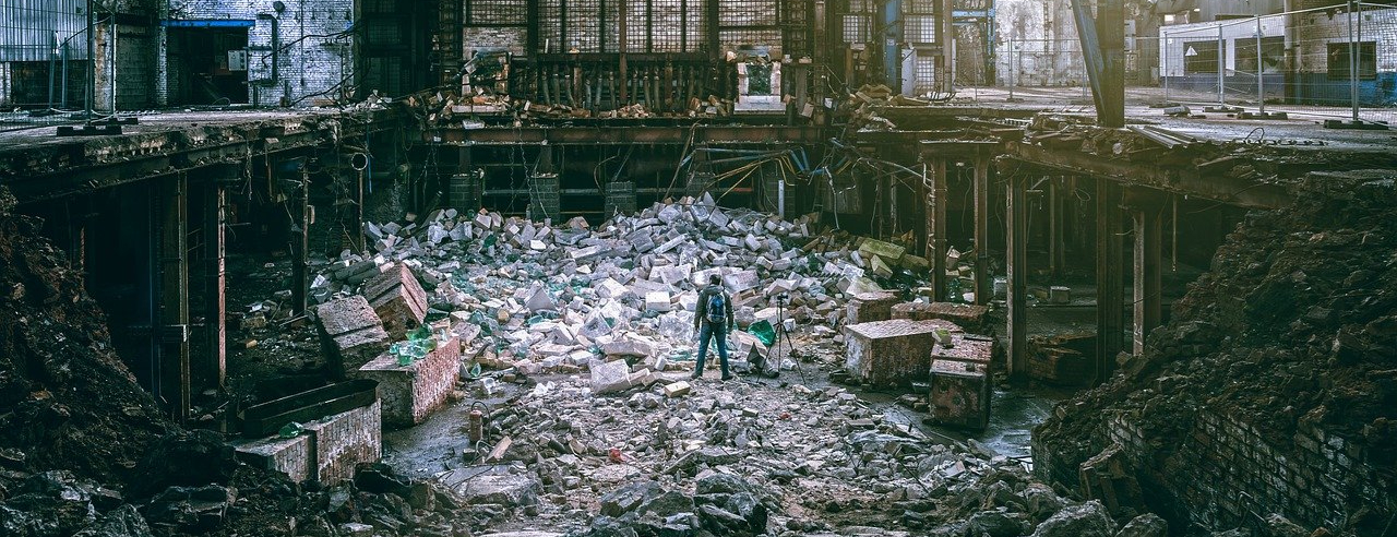 A lone man stands in the debri of an abandoned factory filled with destruction