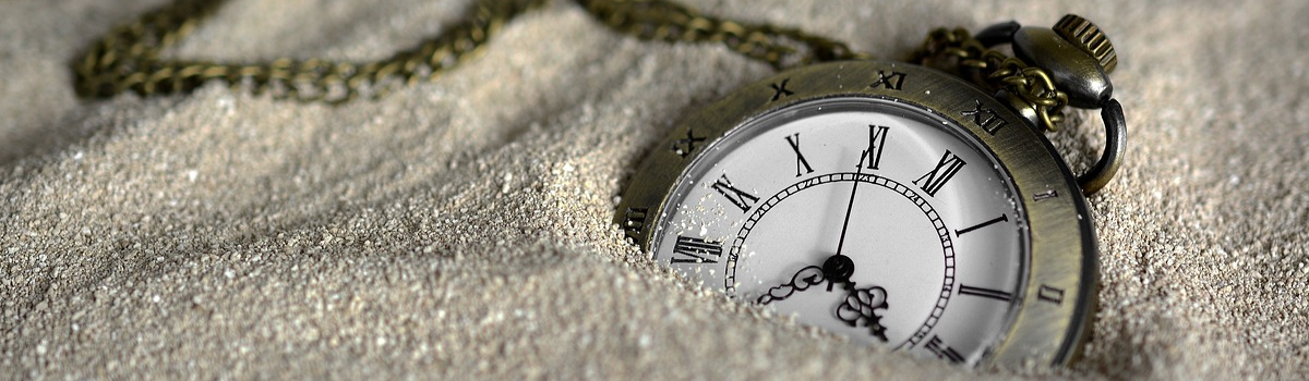 A pocket watch lies partially buried in the sand.
