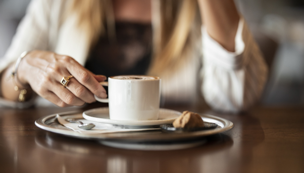 A close up image of a woman's hand holding a coffee cup. She is talking, which is evident by the gesture of her other hand.