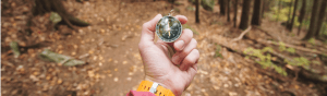 Image of a hand, palm up, holding a compass over a dirt path.