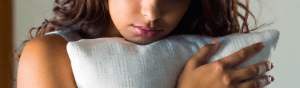 Close up of a woman hugging a pillow. only the bottom portioin of her face is visible.